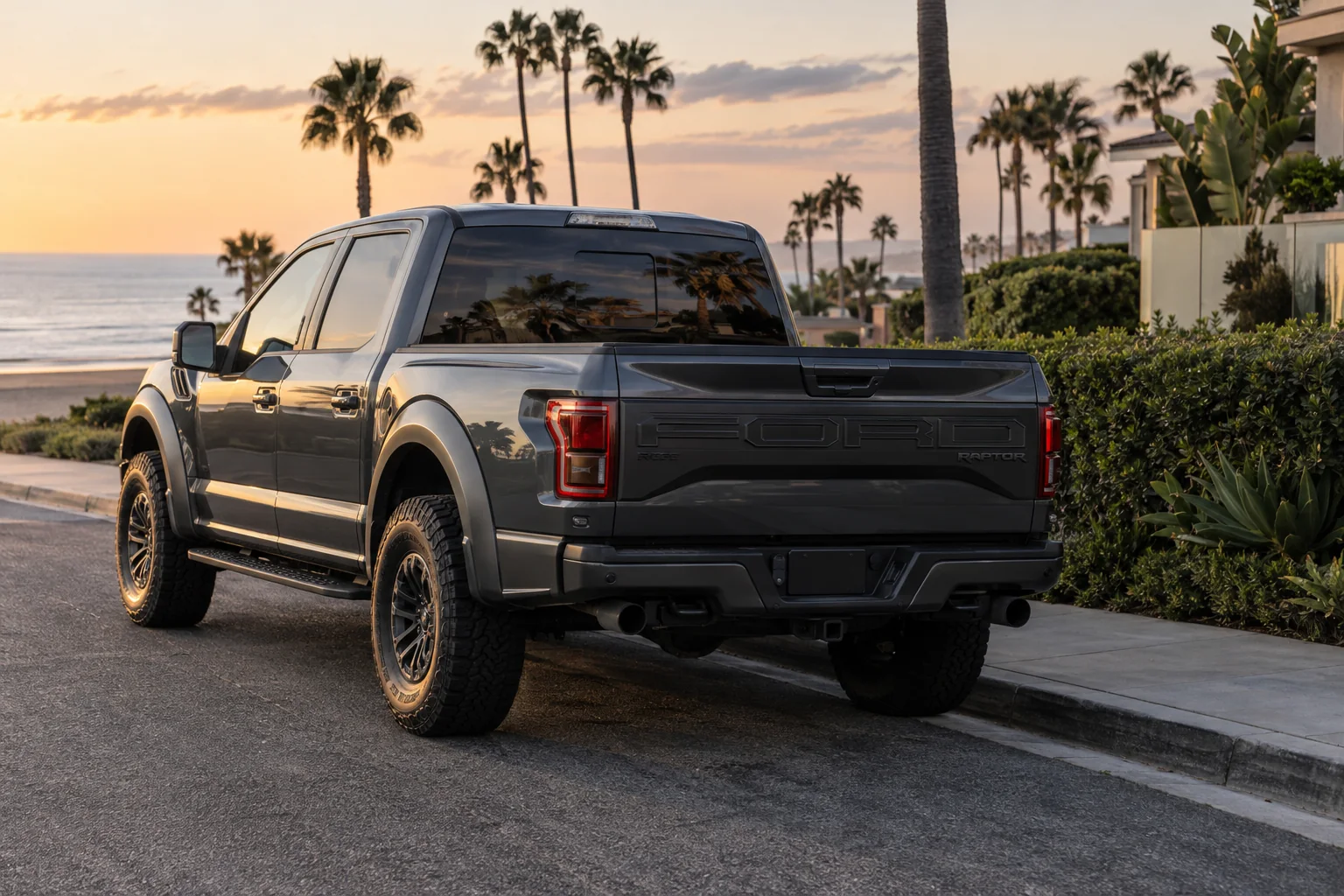 A gray Ford F-150 Raptor with a tinted back window parked by the beach at sunset
