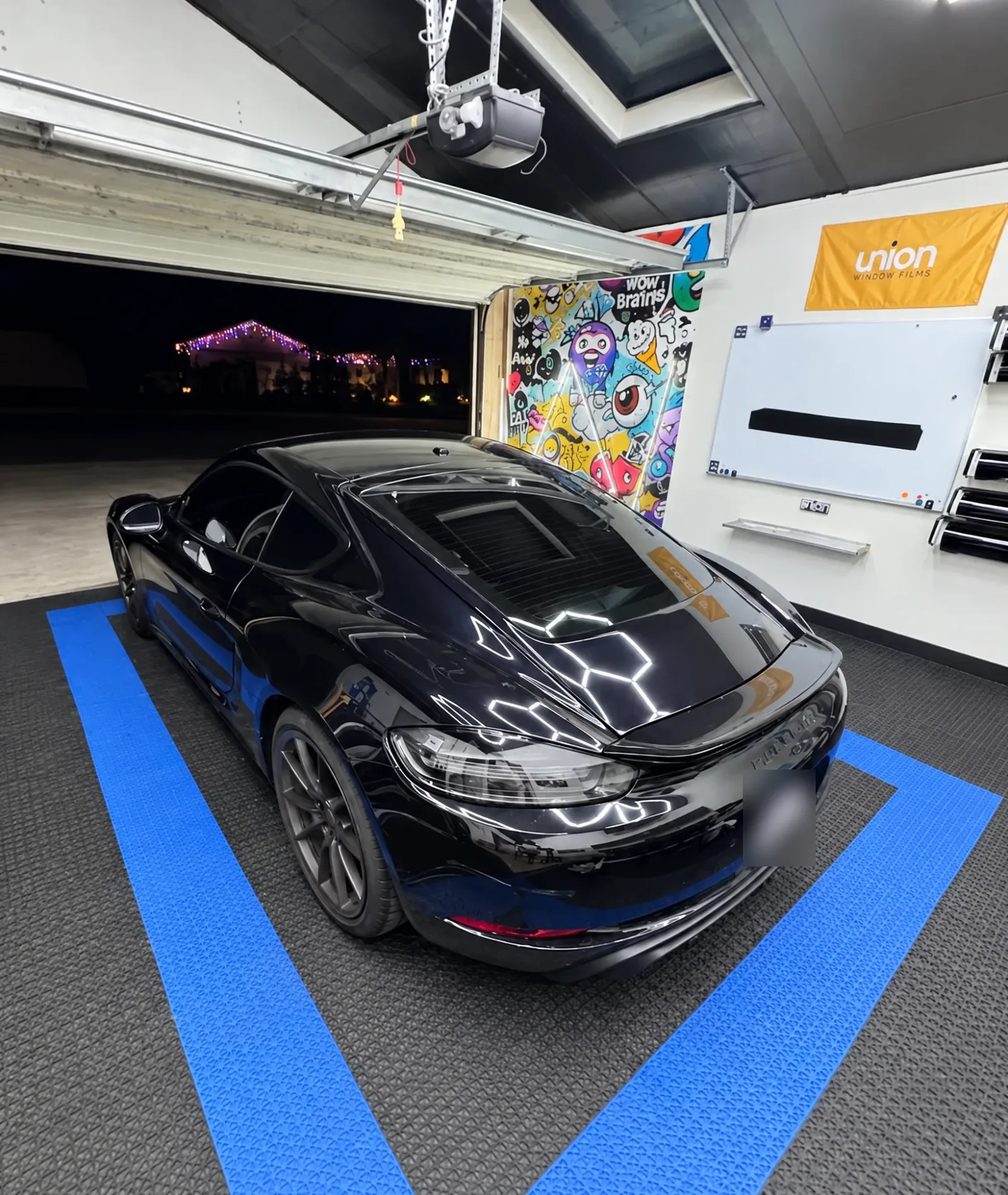 The back of a black Porsche 718 Cayman with tinted windows in the Tint-One workshop at night